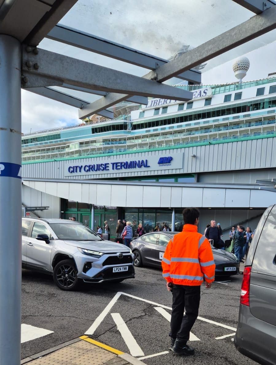 The glazed canopy and sign of a cruise terminal, with a docked cruise ship behind.